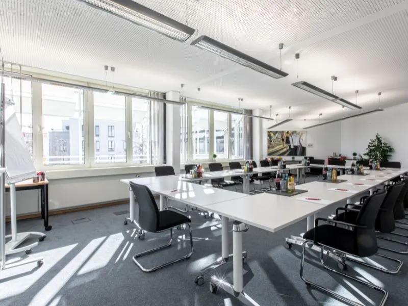 Salle de conférence lumineuse et moderne au Business Campus Mainz, configurée pour une réunion avec des tables en U et chaises ergonomiques.
