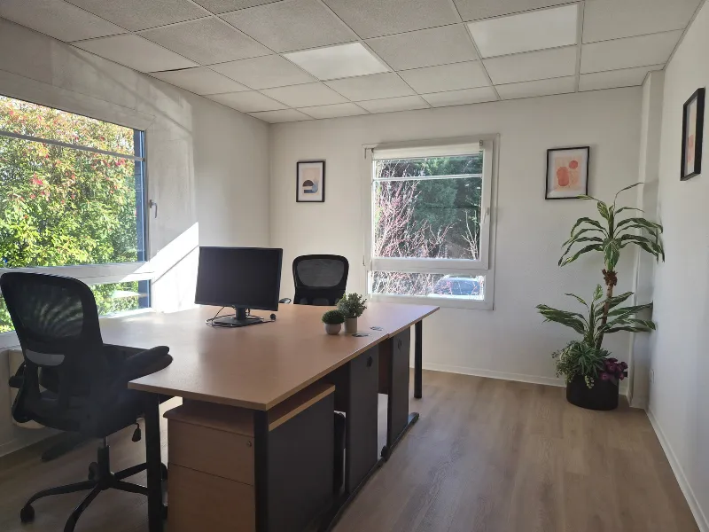 Bureau privatif lumineux et entièrement meublé avec deux postes de travail, chaises ergonomiques et vue sur la verdure.
