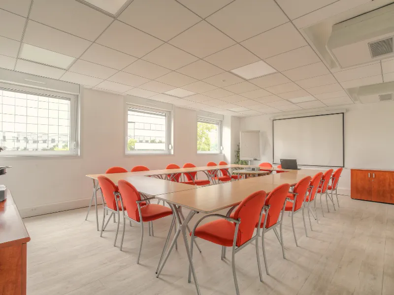 Espace de travail collaboratif et salle de séminaire spacieuse avec lumière naturelle et mobilier modulable.