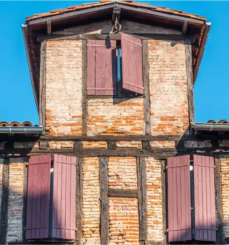 Façade traditionnelle albigeoise à colombages et briques rouges, dotée d'une poulie ancienne et de volets en bois.