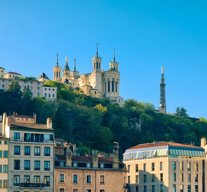 Vue en contre-plongée sur la colline de Fourvière avec la Basilique Notre-Dame de Fourvière et la Tour métallique de télécommunications sous un ciel bleu pur.