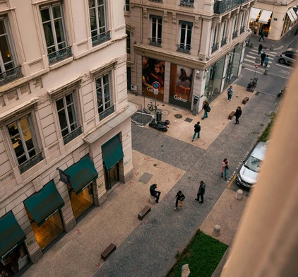 Vue en plongée d'une rue piétonne animée de Lyon, bordée d'immeubles bourgeois aux façades claires et de boutiques élégantes.