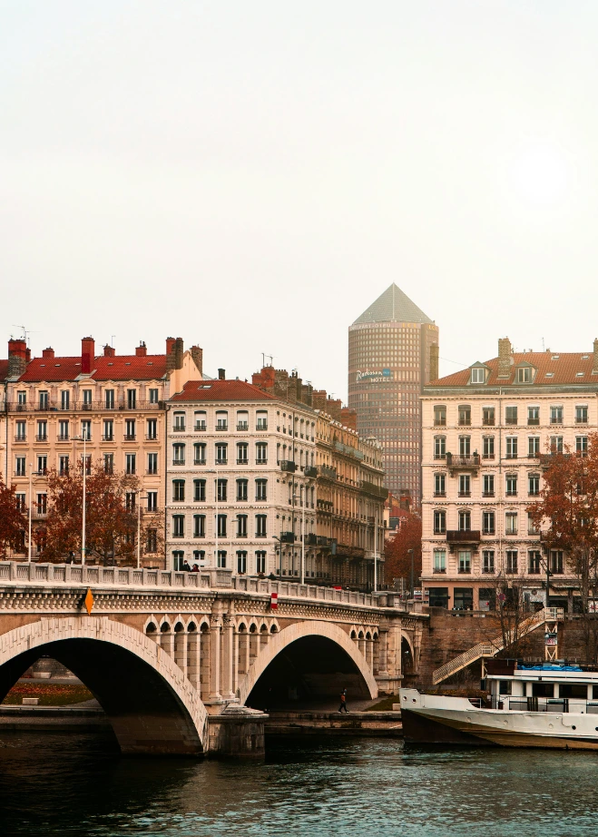 Tour Part-Dieu Vue depuis les quais du Rhône montrant le pont Wilson au premier plan, des façades d'immeubles classiques et la tour Incity (le "Crayon") qui se détache dans la brume en arrière-plan.