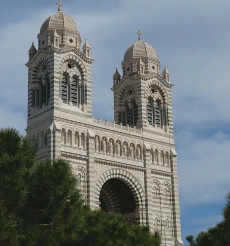 The ornate facade and distinctive domes of Marseille's Cathedral de la Major, surrounded by Mediterranean vegetation, a historic monument close to your coworking space in Marseille.