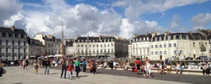 Promeneurs sur l'esplanade animée du port de plaisance de Vannes, face aux bâtiments historiques et terrasses de la place Gambetta.