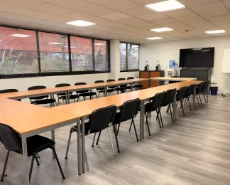 Grande salle de réunion lumineuse avec tables en U, une vingtaine de chaises, écran TV et paperboard – BURO Club Bordeaux Mérignac