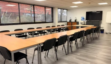 Grande salle de réunion lumineuse avec tables en U, une vingtaine de chaises, écran TV et paperboard – BURO Club Bordeaux Mérignac