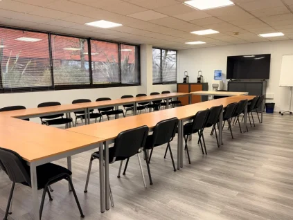 Grande salle de réunion lumineuse avec tables en U, une vingtaine de chaises, écran TV et paperboard – BURO Club Bordeaux Mérignac