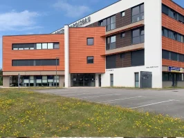 Façade du centre BURO Club Vannes Laroiseau : immeuble de bureaux moderne orange et blanc, avec parking et pelouse fleurie au premier plan.