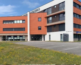 Façade du centre BURO Club Vannes Laroiseau : immeuble de bureaux moderne orange et blanc, avec parking et pelouse fleurie au premier plan.