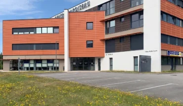 Façade du centre BURO Club Vannes Laroiseau : immeuble de bureaux moderne orange et blanc, avec parking et pelouse fleurie au premier plan.