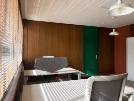 Bureau privatif lumineux avec revêtement mural en bois, porte verte, et bureau blanc équipé d'un écran acoustique près d'une fenêtre à stores vénitiens.