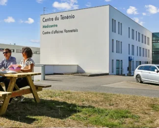 Façade du centre BURO Club Vannes Ténénio : immeuble blanc aux enseignes Centre du Ténénio et Centre d'affaires Vannetais ; deux personnes à une table de pique-nique sur la pelouse.