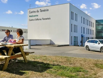 Façade du centre BURO Club Vannes Ténénio : immeuble blanc aux enseignes Centre du Ténénio et Centre d'affaires Vannetais ; deux personnes à une table de pique-nique sur la pelouse.
