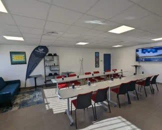 Salle de réunion spacieuse chez BURO Club Partner Aix Éguilles, configurée en U avec chaises rouges, écran interactif et coin lounge.