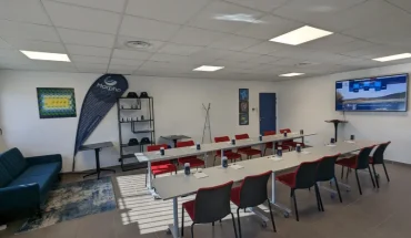 Salle de réunion spacieuse chez BURO Club Partner Aix Éguilles, configurée en U avec chaises rouges, écran interactif et coin lounge.