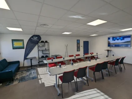 Salle de réunion spacieuse chez BURO Club Partner Aix Éguilles, configurée en U avec chaises rouges, écran interactif et coin lounge.