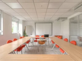 Grande salle de réunion équipée avec écran de projection et tableau blanc, disposition en U idéale pour les formations.