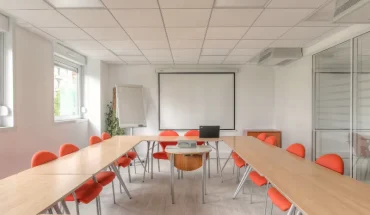 Grande salle de réunion équipée avec écran de projection et tableau blanc, disposition en U idéale pour les formations.