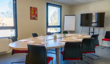 Salle de réunion avec table ovale, écran TV et paperboard au BURO Club Le Mans