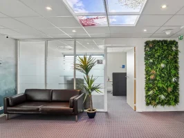 Espace d'attente du centre BURO Club Vannes Laroiseau, avec canapé en cuir brun, mur végétal, cloisons vitrées et plafond imitant un ciel.