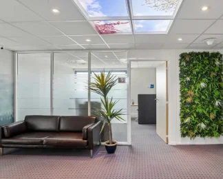 Espace d'attente du centre BURO Club Vannes Laroiseau, avec canapé en cuir brun, mur végétal, cloisons vitrées et plafond imitant un ciel.