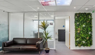 Espace d'attente du centre BURO Club Vannes Laroiseau, avec canapé en cuir brun, mur végétal, cloisons vitrées et plafond imitant un ciel.