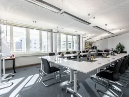 Salle de conférence lumineuse et moderne au Business Campus Mainz, configurée pour une réunion avec des tables en U et chaises ergonomiques.