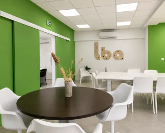 Espace partagé au BURO Club Partner Beaune avec murs verts, table ronde en bois, grande table de réunion et portes coulissantes.