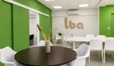Espace partagé au BURO Club Partner Beaune avec murs verts, table ronde en bois, grande table de réunion et portes coulissantes.