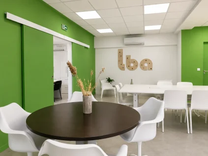 Espace partagé au BURO Club Partner Beaune avec murs verts, table ronde en bois, grande table de réunion et portes coulissantes.