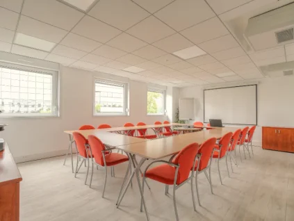 Espace de travail collaboratif et salle de séminaire spacieuse avec lumière naturelle et mobilier modulable.