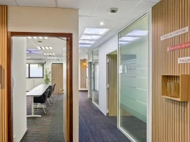 Couloir habillé de lattes de bois au centre BURO Club Vannes Laroiseau, ouvert sur une salle de réunion et des bureaux vitrés, avec panneaux « Espace de coworking » et « Pause ».