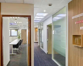 Couloir habillé de lattes de bois au centre BURO Club Vannes Laroiseau, ouvert sur une salle de réunion et des bureaux vitrés, avec panneaux « Espace de coworking » et « Pause ».