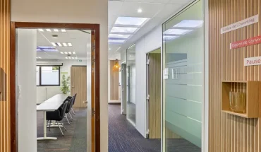 Couloir habillé de lattes de bois au centre BURO Club Vannes Laroiseau, ouvert sur une salle de réunion et des bureaux vitrés, avec panneaux « Espace de coworking » et « Pause ».
