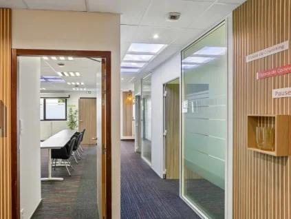 Couloir habillé de lattes de bois au centre BURO Club Vannes Laroiseau, ouvert sur une salle de réunion et des bureaux vitrés, avec panneaux « Espace de coworking » et « Pause ».