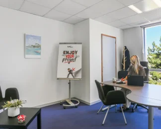 Bureau privatif du centre BURO Club Vannes Ténénio : une femme travaille sur ordinateur portable face à une fenêtre, à côté d'un paperboard et d'un coin salon.