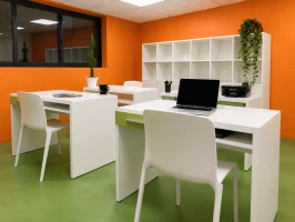 Espace de coworking au BURO Club Partner Beaune avec murs orange, sol vert, postes de travail blancs individuels et rangements.