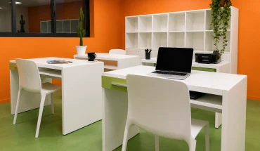 Espace de coworking au BURO Club Partner Beaune avec murs orange, sol vert, postes de travail blancs individuels et rangements.
