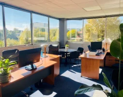 Bureau d'angle pour 3 personnes avec grandes baies vitrées, table de réunion et vue sur la verdure