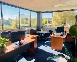 Bureau d'angle pour 3 personnes avec grandes baies vitrées, table de réunion et vue sur la verdure