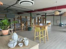 Espace détente et tisanerie d'un espace de travail partagé, présentant un service à thé au premier plan, une table haute jaune avec tabourets et un coin salon en arrière-plan.