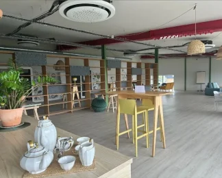 Espace détente et tisanerie d'un espace de travail partagé, présentant un service à thé au premier plan, une table haute jaune avec tabourets et un coin salon en arrière-plan.