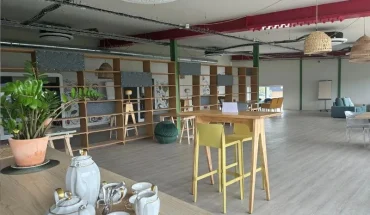Espace détente et tisanerie d'un espace de travail partagé, présentant un service à thé au premier plan, une table haute jaune avec tabourets et un coin salon en arrière-plan.