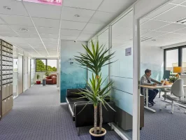 Couloir du centre BURO Club Vannes Laroiseau avec casiers à courrier, canapé en cuir noir et bureau vitré où un homme travaille sur ordinateur.