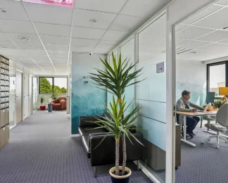 Couloir du centre BURO Club Vannes Laroiseau avec casiers à courrier, canapé en cuir noir et bureau vitré où un homme travaille sur ordinateur.