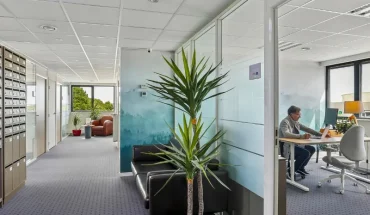 Couloir du centre BURO Club Vannes Laroiseau avec casiers à courrier, canapé en cuir noir et bureau vitré où un homme travaille sur ordinateur.