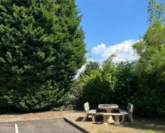 Espace de détente extérieur aménagé avec une table et des bancs en pierre au milieu des arbres.