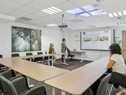 Salle de réunion du centre BURO Club Vannes Laroiseau, avec tables en U et vidéoprojecteur ; un intervenant présente un écran à deux participantes.