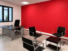 Bureau de direction au BURO Club Partner Beaune avec mur d'accent rouge, bureau en bois foncé et espace d'accueil avec fauteuils noirs.